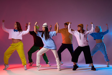 Active young group of people standing synchronically on floor of studio dance, raising fists up, looking at right side together, exercising new movie in street dance