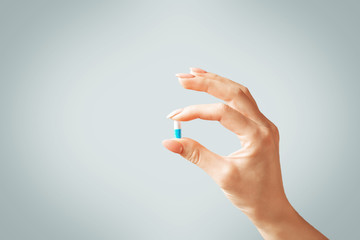 Female hand holding a capsule pill or vitamin. - 302059799