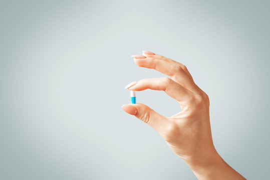 Female hand holding a capsule pill or vitamin.