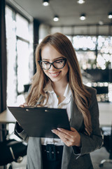 Beautiful female office employee in glasses smiling and looking into her clipboard