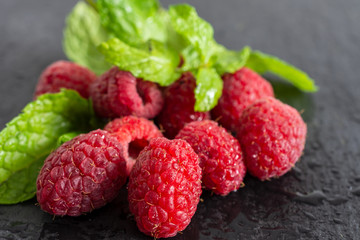Top view of wet raspberries with mint leaves out of focus on black slate