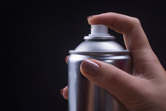Female hand holds an aerosol can on a black background.