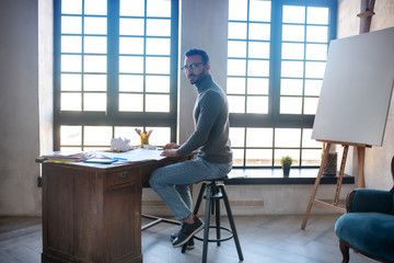 Designer wearing glasses sitting at the table near drawing easel