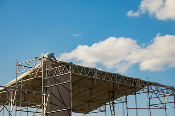 music stage steel pipes frame installation process by worker person, blue sky white clouds background clear day time and empty copy space for your text here 