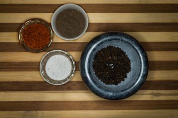 Spices red ground pepper, black ground pepper, salt, peas and peas in a pepper mill on a wooden shelf close-up