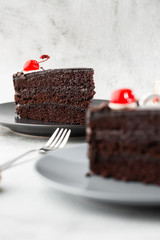 A slice of delicious chocolate cake with cherry on top on marble background. Piece of Cake on a Plate. Sweet food. Sweet dessert. Close up. Cafe menu. vertical photo.