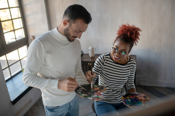 Smiling girlfriend taking paints while painting with beloved