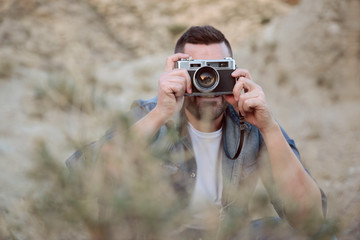 Hombre joven con cámara de fotos analógica tomando fotos escondido detrás de unos arbustos