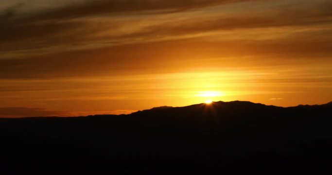 Brilliant orange sunset over desert mountain fast motion. Brilliant orange sunset over desert mountain. Late evening orange golden sun sets over desert mountain peaks in southern Utah near St George.