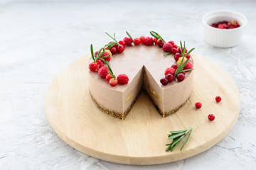 Raw cake decorated with raspberries and rosemary on a wooden board. Gluten free, vegetarian food.