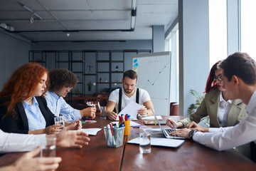 Young caucasian creative people sitting at table in modern office and discussing new projects together