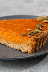 Portion of delicious bright orange pumpkin open pie on gray plate, decorated with pumpkin seeds with dessert forks close-up, top view. Bright marble background. Copy space. Vertical. menu for cafe