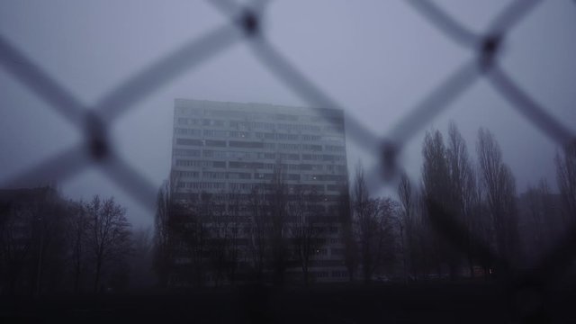 Urban city backgrounds. Multi-storey building in the morning, in the fog. Apartment building behind bars. Ghetto, housing the poor. Concept: restriction of freedom