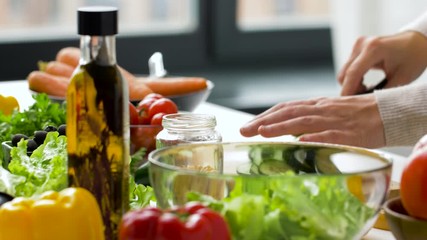 healthy eating, vegetarian food and cooking concept - young woman making vegetable salad and chopping cucumber with kitchen knife on wooden cutting board at home - Powered by Adobe