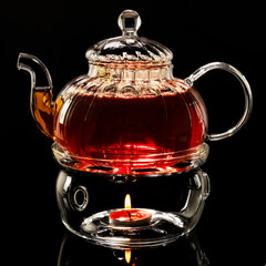 glass teapot on a glass stand heated by a candle on a black background, black tea in a glass teapot isolated on a black background