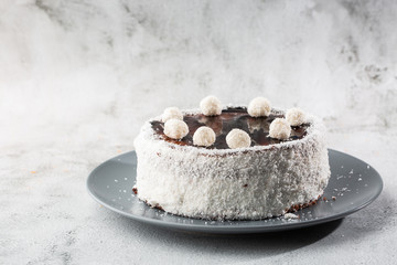 Delicious whole chocolate cake on plate with coconut candies on top on table on marble background. Wallpaper for pastry cafe or cafe menu. horizontal.