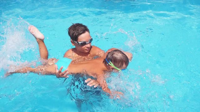 Child teach his little boy Brother to swim in the pool, the boy moves his arms and legs and laughs. Slow motion. Family having fun in the pool in summer. Summer holiday.