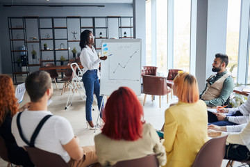 black businesswoman stand talking explaining making flip chart presentation for office employees using diagrams, motivated african American speaker coach present business plan