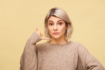 Human facial expressions and body language. Positive good looking young blonde female holding hand at his ear imitating cell phone, saying Call me, I will be in touch, posing isolated in studio