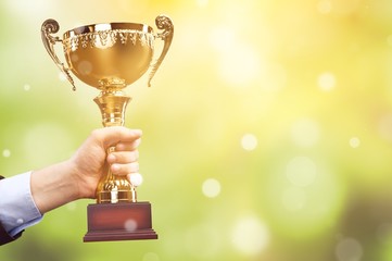 Hand holding golden trophy on background