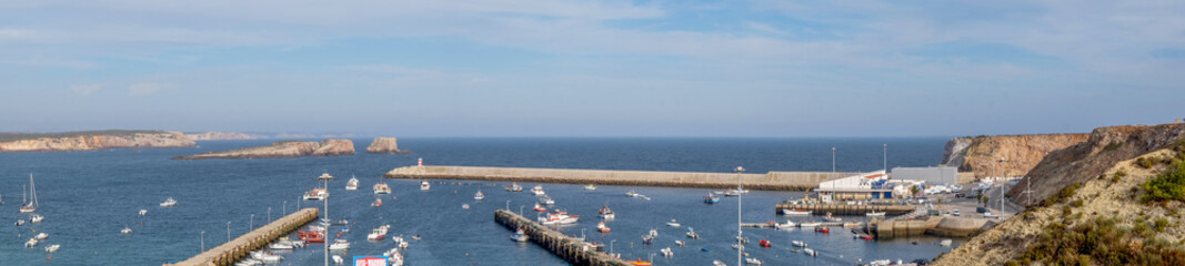 Fototapeta premium Panorama of Sagres Harbour, Algarve, Portugal, harbour boats and the harbour wall with cliffs and rocks behind