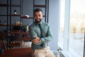 portrait of confident young handsome middle eastern businessman standing in office, looking at...