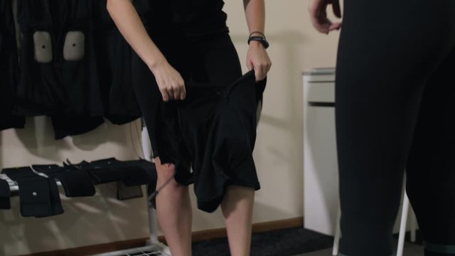 girl sticks her legs and puts on a special suit for EMC training, the trainer helps the girl