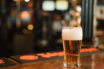 a glass of beer in a popular bar. Pint of foamy drink in a restaurant. Mug with beer at the bar counter