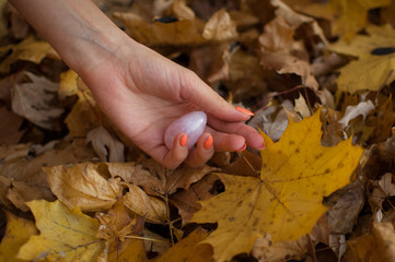 Female hand with orange manicure holding pink quartz yoni egg for vumfit, imbuilding or meditation...