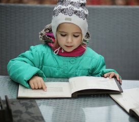 Three year old girl reading a menu in the outdoor cafe terrace