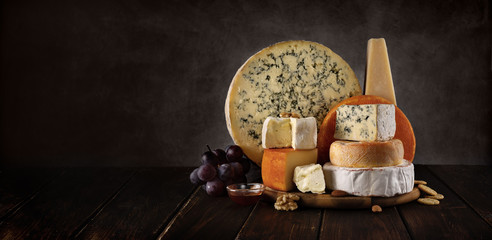 Variety of cheeses on a wooden board with nuts and honey