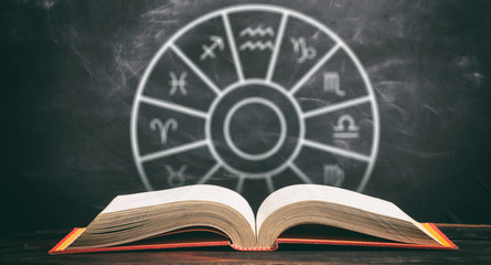 Zodiac signs set over an open book, black background.
