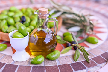 Fresh green olives with branches and leaves. Seasonal harvest in Italy. Bottle of olive oil and...