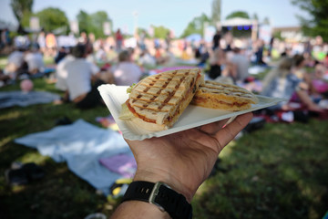 Festival food, dinner, eating and people concept - hand with panini sandwich with tomatoes and cheese at festival
