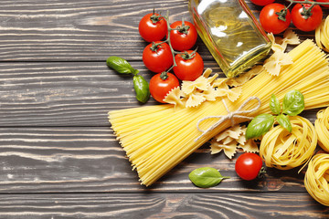 Composition with different Uncooked pasta, ingredients for sauce. cherry tomatoes,  spices, oil, basil on a wooden background. top view. Place for text.