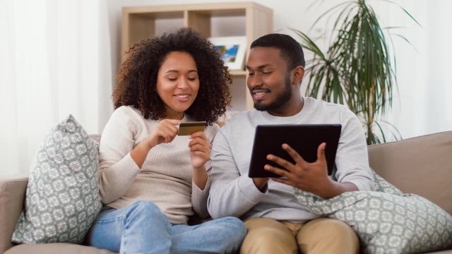 family, technology, online shopping and people concept - happy african american couple couple with tablet pc computer and credit card at home
