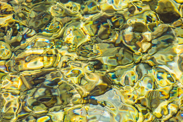 Abstract background of clear sea or river water ripple waves in light green khaki color. Sea water with different color pebbles at the bottom. Sun reflection on sea water surface. © sunday_morning
