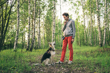 Naklejka na ściany i meble Young guy teaching dog to give paw at forest
