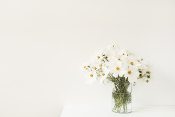 Fototapeta na wymiar A beautiful background with white chamomile, daisy flowers in vase standing on white table. Holiday, wedding, birthday, anniversary concept.