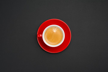 Hot creamy espresso coffee in red cup with saucer isolated on black office desk