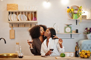 Two african american female friends women spending time at kitchen with wine. Black girlfriends  relaxing at home.