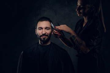 Talented hairdresser is making nice haircut for customer man at dark studio.