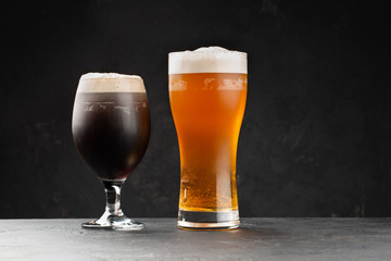 Dark and light cold foamy beer in classic pub glasses on black background