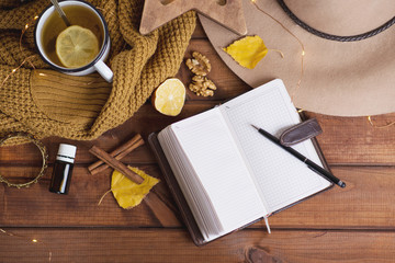 The concept of a cozy retro photo in autumn style. A notebook for recording desires and plans, a warm sweater and tea with lemon and cinnamon in a cozy house. Magical beautiful photo on a dark wood ta