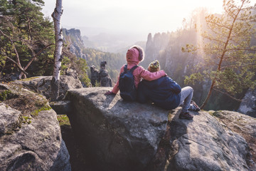 Young couple in outdoor clothing with backpacks resting after hike on limestone rock enjoying back...