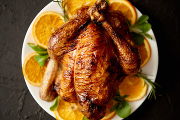 Roasted whole chicken or turkey served in white ceramic plate with oranges