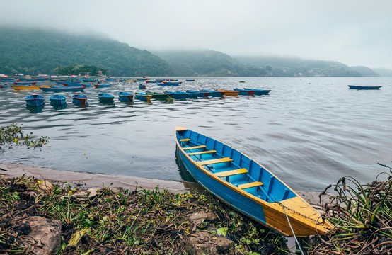 Multicolored traditional rowboats on the morning lake water in Pokhara, Gandaki Pradesh, Nepal. Asian traveling concept image.