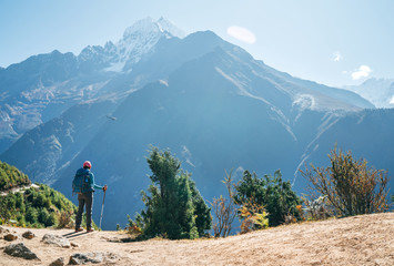 Young hiker backpacker man using trekking poles enjoying the Thamserku 6608m mountain with flying rescue helicopter during high altitude Acclimatization walk. Everest Base Camp trekking route, Nepal.