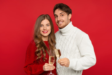 smiling couple clinking champagne glasses and looking at camera isolated on red background. Christmas concept