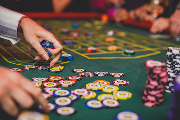 A close-up vibrant image of multicolored casino table with roulette in motion, with casino chips. the hand of croupier, mone and a group of gambling rich wealthy people in the background